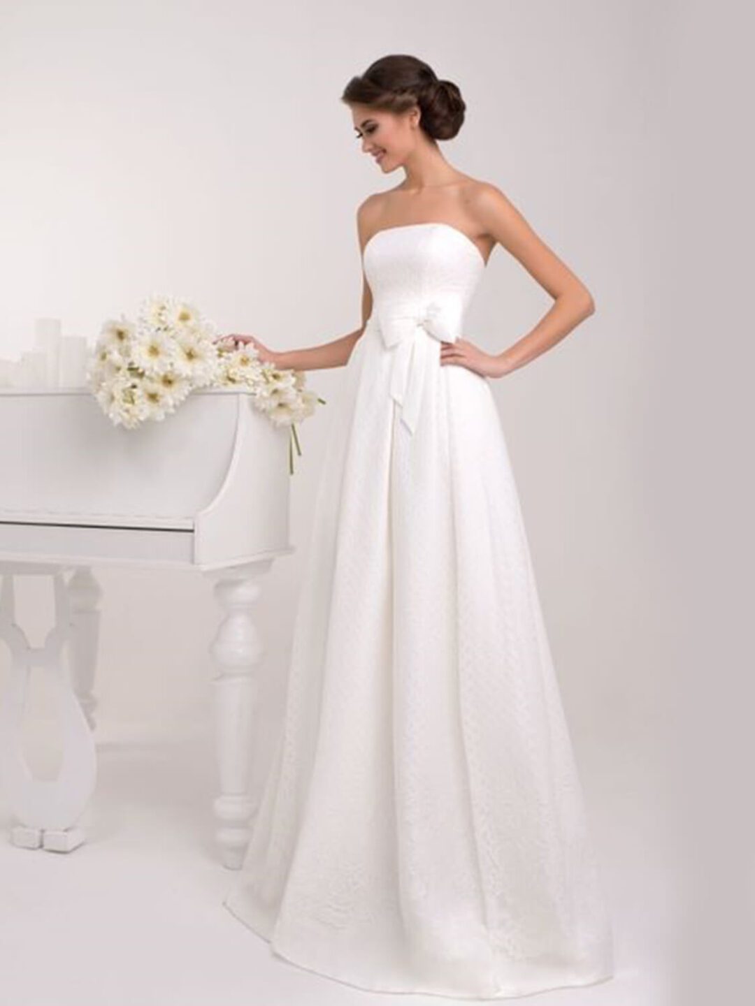 Στράπλες  νυφικό σε Άλφα γραμμή με υπέροχο δέσιμο στη μέση με πλούσιο φιόγκο. Σε ανάγλυφο γαλλικό σατέν. Υπέροχο δέσιμο με κορδέλα στην πλάτη σε στυλ κορσέ.